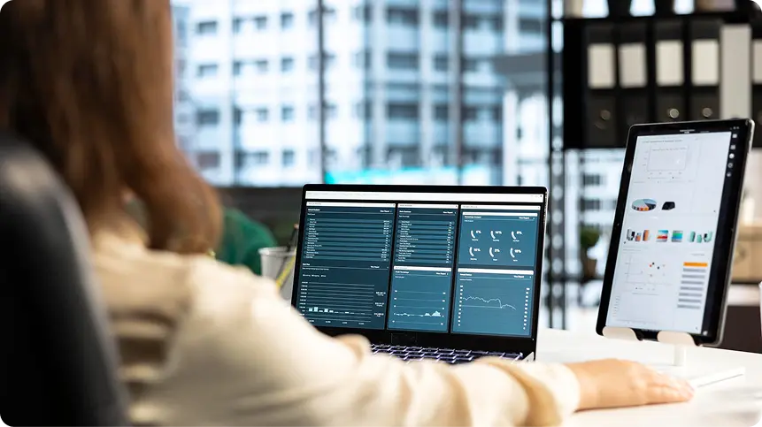 Woman comparing dashboards on a laptop and a tablet side by side at an office desk