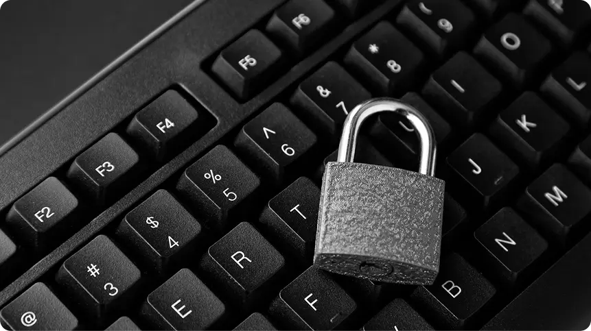 Closed metal padlock resting on the keys of a black keyboard, shot close-up
