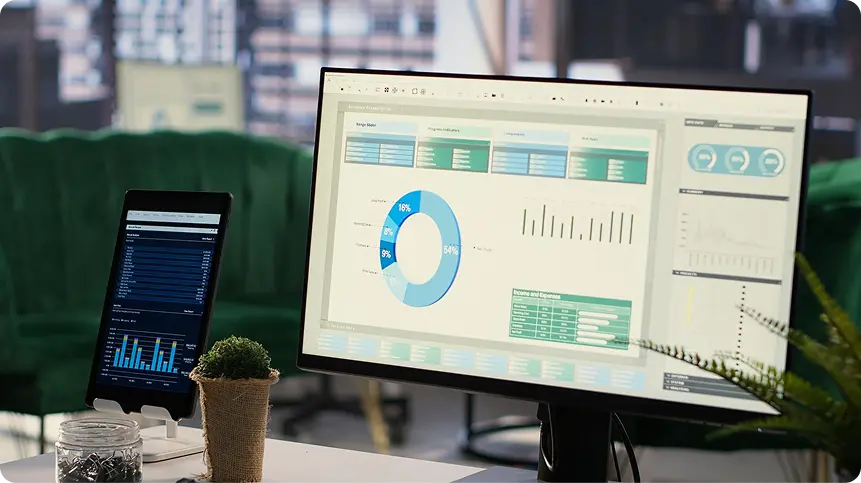 Monitor on a desk showing a dashboard with a donut chart, bar charts, and data tables