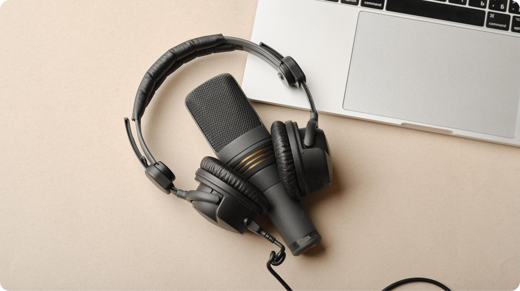 Micrófono de condensador y audífonos de estudio junto a una laptop, equipo básico para producir un podcast