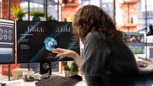 Analista de datos señala gráficos de rendimiento en un panel con dos monitores de oficina
